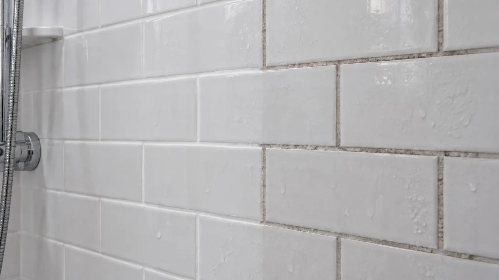 Mur de douche en carrelage blanc avec des joints propres d'un côté et noircis de l'autre